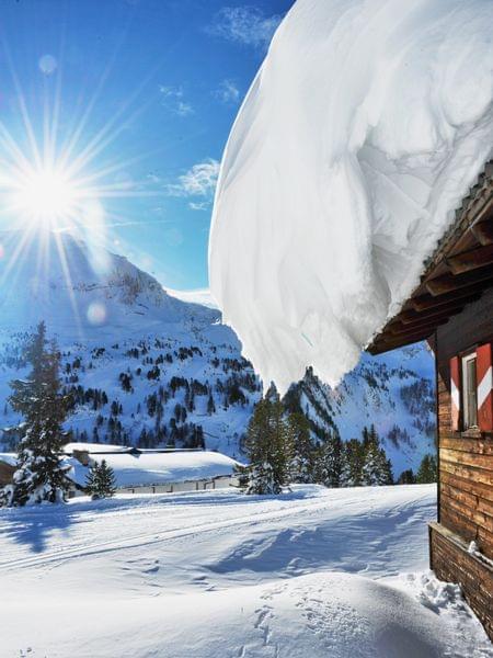 Flockenzauber im Winter in Obertauern. Schneebedeckte Almhütte in sonniger Winterberglandschaft